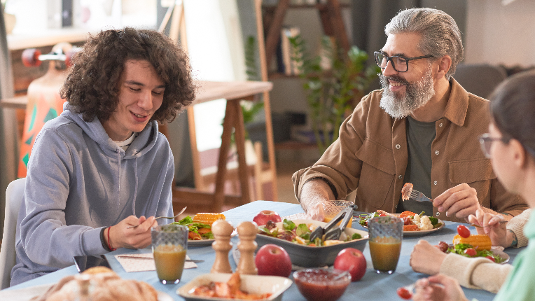 Happy family talking to each other while sitting at the table and having dinner at home.