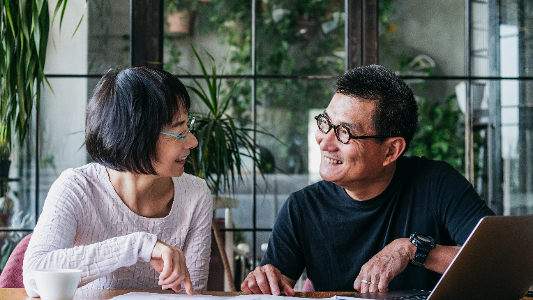 Mature and senior man and woman sitting at table, with home finances, using computer, cheerful and happy.