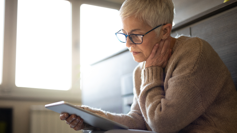 Serious senior woman using tablet computer indoors seems concerned.