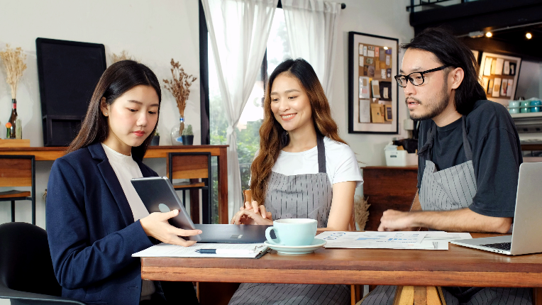 Young Asian business woman discussing financial planning with small business owner at cafe coffee shop.