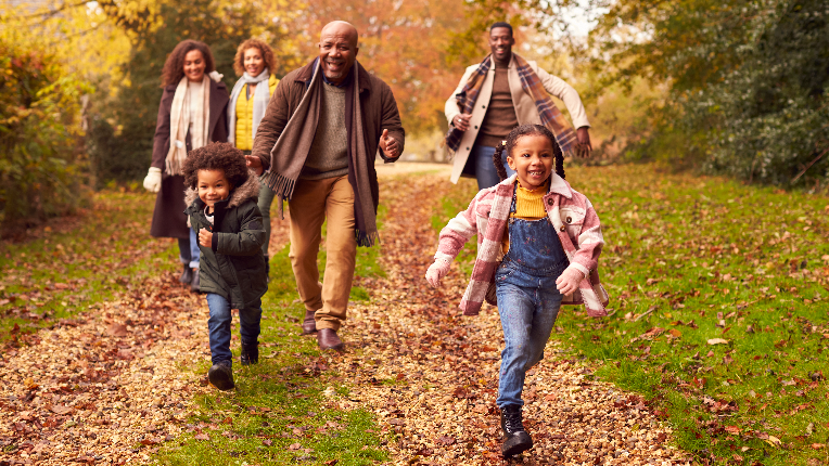 Smiling Multi-Generation Family Having Fun With Children Walking Through Autumn Countryside Together.