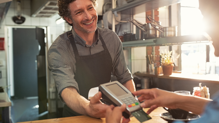 Franchise worker holding debit machine for customer who is making is a payment with their bank card.