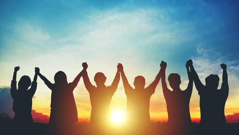 Silhouette of group making high hands over head in sunset sky